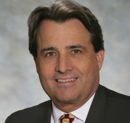 A middle-aged man with dark hair wearing a dark suit, light shirt, and patterned tie poses for a professional headshot against a neutral background, representing Chicago lawyers experienced in litigation support.