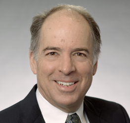 A middle-aged man with thinning gray hair, wearing a dark suit, light shirt, and patterned tie, smiles at the camera in front of a neutral background—a professional image often seen in law offices or among top Chicago lawyers.