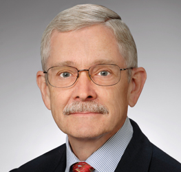 An older man with gray hair, glasses, and a mustache is wearing a suit, striped shirt, and patterned red tie—presenting the polished look of lawyers in Chicago against a neutral background.