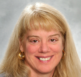 A woman with long blonde hair, wearing gold hoop earrings, smiles at the camera against a gray background, reflecting the confidence often seen in lawyers in Chicago.