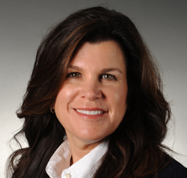 Woman with long brown hair, dressed in a white collared shirt and dark blazer, smiles at the camera against a gray background—representing the professionalism of Chicago lawyers.