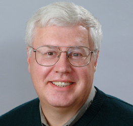 A middle-aged man with short white hair, glasses, and a sweater smiles at the camera against a plain light background, embodying the approachable professionalism of Chicago lawyers.