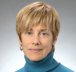 A woman with short blonde hair, wearing a blue turtleneck sweater and gold hoop earrings, poses in front of a plain gray background—reflecting the professionalism often seen at top Chicago lawyers' law offices.
