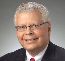 Middle-aged man with short gray hair, glasses, and a suit with a red tie, smiling at the camera—a professional look often seen in law offices specializing in intellectual property law.