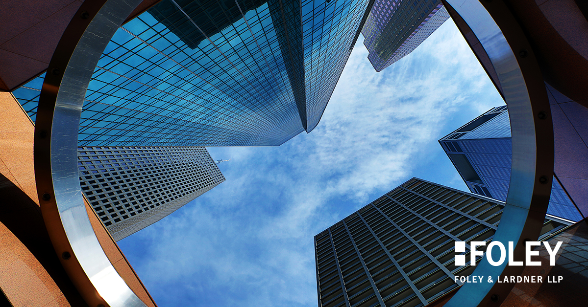 View looking up at modern skyscrapers through a circular architectural structure, under a blue sky with scattered clouds. Showcasing corporate law office excellence, text reads "FOLEY FOLEY & LARDNER LLP" in the bottom right corner.