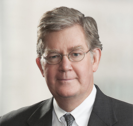 A middle-aged man wearing glasses, a dark suit, white shirt, and striped tie poses against a neutral, blurred background—reflecting the professionalism found in leading corporate law offices.