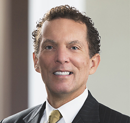 A man in a dark pinstriped suit, white shirt, and yellow tie, smiling with short curly hair, poses in a professional indoor setting—ideal for representing lawyers in Chicago or intellectual property law firms.