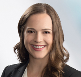 A woman with long brown hair, wearing a black blazer and white top, smiles at the camera against a light background, reflecting the professionalism found in leading corporate law office teams.