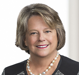 A middle-aged woman with short, light brown hair is smiling. She wears a pearl necklace, earrings, and a black and gray top, posed against a plain background—reflecting the professionalism found in leading Chicago lawyers.