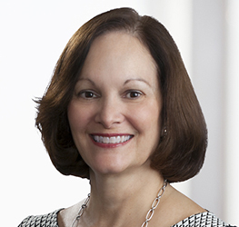 A woman with short brown hair smiles at the camera, wearing a patterned top and a silver necklace. The softly blurred background suggests a friendly, approachable atmosphere often found among lawyers in Chicago.