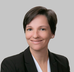 A person with short dark hair wearing a black blazer and white shirt, smiling in front of a plain light gray background—perfect for showcasing professionals at a corporate law office or lawyers in Chicago offering litigation support.