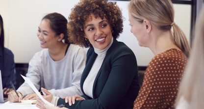 Four women sit around a table in a law office setting, engaged in conversation and collaborating on intellectual property law matters, with a laptop and documents visible.