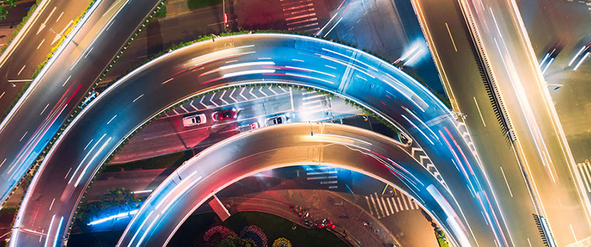 Aerial view of a brightly lit highway interchange at night, showing curved overpasses and moving vehicle light trails—mirroring the dynamic energy of lawyers in Chicago navigating complex city roads below.