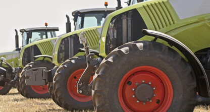 A row of green tractors with large red wheels is lined up on dry grass in an outdoor setting, much like lawyers in Chicago, ready to offer steadfast litigation support when it's needed most.
