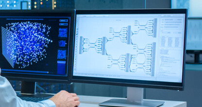 A person sits at a desk in a corporate law office, using two computer monitors displaying data visualizations and complex diagrams in a modern office setting.