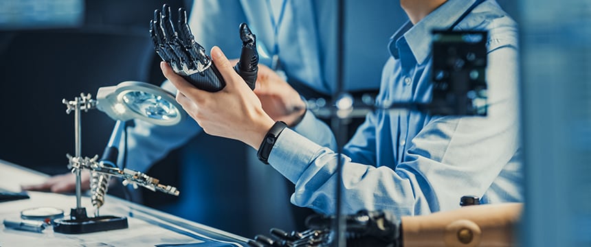 A person examines a robotic hand at a desk equipped with tools, a magnifying lamp, and electronic components—mirroring the precision found in litigation support often utilized by law offices and lawyers in Chicago.