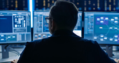 Person sitting at a desk with multiple computer monitors displaying code, data charts, and network diagrams in a dimly lit office, focused on providing litigation support for chicago lawyers.