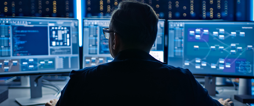 Person sitting at a desk with multiple computer monitors displaying code, data charts, and network diagrams in a dimly lit office, focused on providing litigation support for chicago lawyers.
