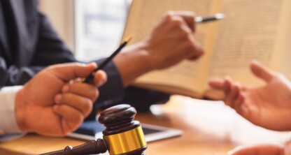 A close-up of hands in a legal meeting with chicago lawyers, a gavel on the table, an open book, and people discussing intellectual property law with pens in hand.