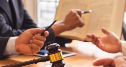 Three people in business attire discuss legal documents at a table with a gavel and open book, capturing the collaborative spirit of a corporate law office.