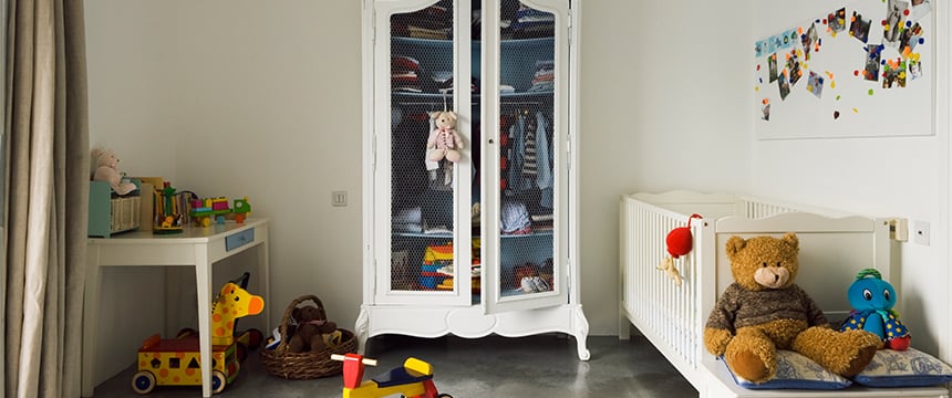A tidy children's room with a crib, stuffed toys, a wardrobe with clothes, a play table with toys, and a wall board displaying photos and artwork—far from the world of corporate law offices or intellectual property law.