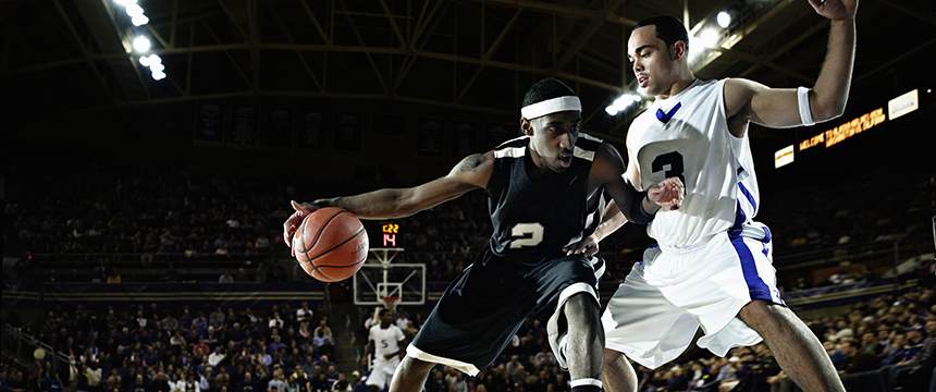 Two basketball players, one in black and one in white, compete for the ball on an indoor court during a game with fans in the background—much like skilled Chicago lawyers battling for their clients.