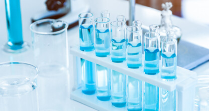A set of test tubes with blue liquid arranged in a white rack on a laboratory table, surrounded by other glassware, evokes the precision often found in intellectual property law offices.