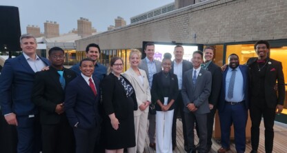 A group of chicago lawyers in business attire stand together smiling on a wooden deck with a brick building in the background, representing a leading corporate law office.
