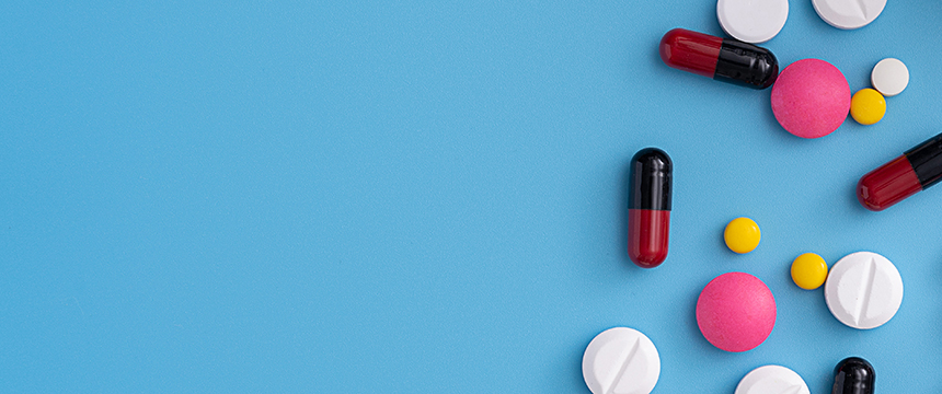 Assorted pills and capsules of various colors and shapes scattered on a blue background, with empty space on the left side, symbolizing complex cases that lawyers in Chicago or a corporate law office might handle.