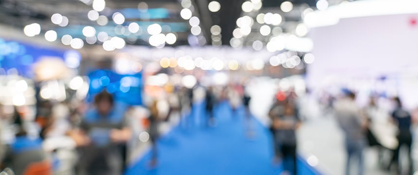 A blurred image of people walking and gathering in a brightly lit indoor event space with a blue carpet, reminiscent of a corporate law office or networking event for lawyers in Chicago.