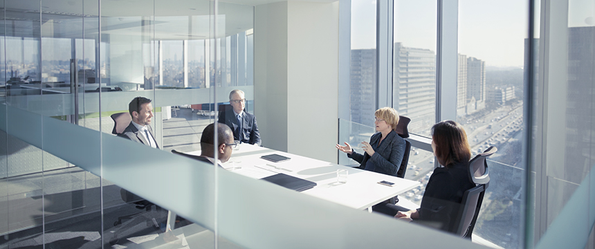 Five people sit around a conference table in a modern corporate law office with large windows overlooking a cityscape, engaged in a business meeting.
