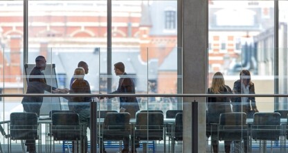 A group of people are meeting around a conference table in a modern law office with large windows overlooking city buildings, discussing intellectual property law and litigation support.