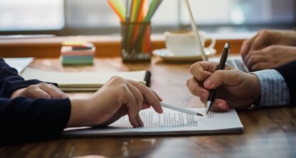 Two people sit at a wooden desk reviewing and signing documents with pens, while Chicago lawyers provide guidance. Office supplies and a cup appear in the background.