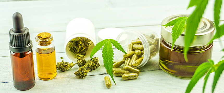 Various CBD products, including oil in dropper bottles, capsules, dried cannabis, and a jar of oil, are arranged on a light wooden surface with cannabis leaves—an image suitable for lawyers in Chicago specializing in intellectual property law.
