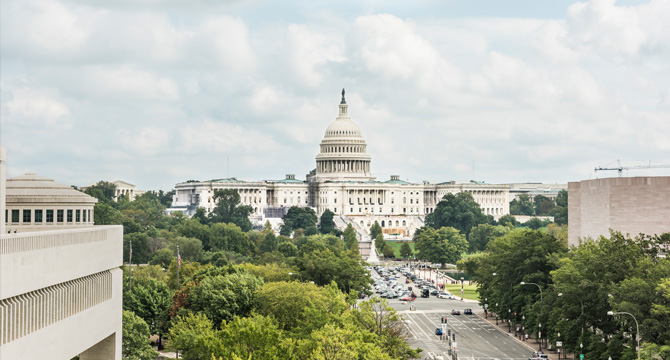 The United States Capitol building is seen in the background, while traffic moves along a tree-lined avenue—an inspiring view for law offices offering trusted litigation support under a partly cloudy sky.