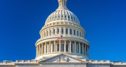 The United States Capitol dome against a clear blue sky, with an American flag flying in front of the building—an inspiring sight for law offices and those seeking litigation support across the nation.
