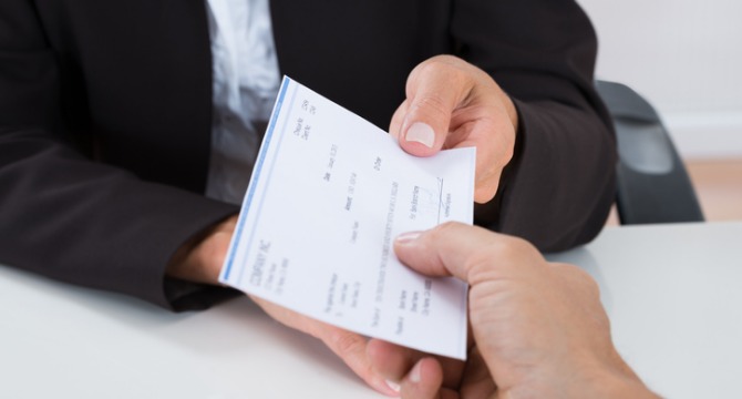A person in a suit hands a check to another across a desk, highlighting litigation support often provided by lawyers in Chicago.