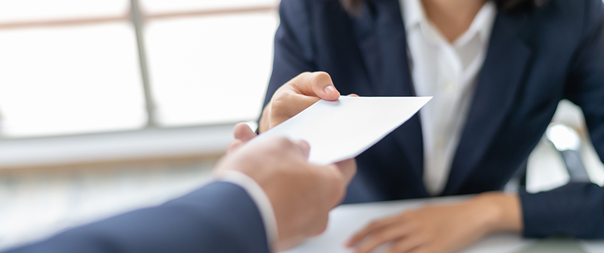 A person in business attire hands an envelope to another across a table, capturing a moment that could take place in a corporate law office or among lawyers in Chicago.