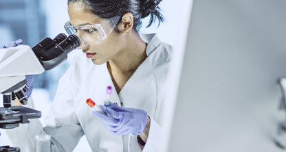 A scientist wearing safety goggles and gloves examines a sample under a microscope, reflecting the precision seen in intellectual property law practices within top law offices.