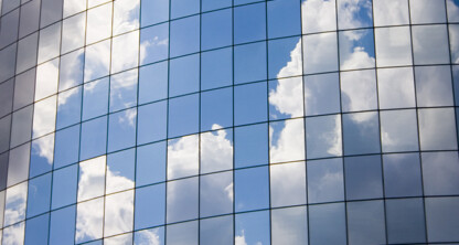 Glass windows on a modern curved corporate law office reflect a blue sky with scattered white clouds.