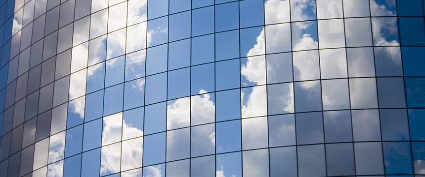 Glass windows on a modern curved corporate law office reflect a blue sky with scattered white clouds.
