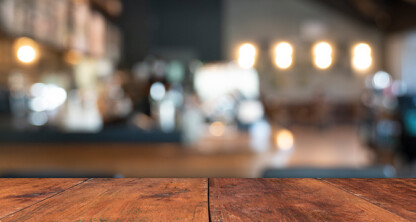 A wooden table in the foreground with a blurred view of a café or restaurant interior resembling modern law offices in the background, featuring lights and furniture.