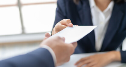 A person in a suit hands an envelope to another individual across a table, capturing a moment often seen in law offices with chicago lawyers handling important legal matters.
