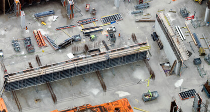 Aerial view of a construction site with concrete slabs, steel beams, scaffolding, and construction materials arranged on the ground near a bustling corporate law office in Chicago.