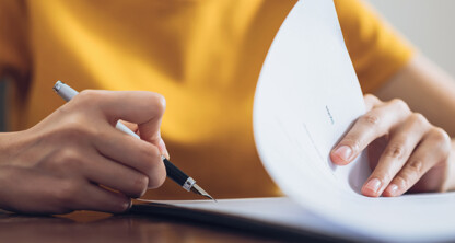In a corporate law office, a person wearing a yellow shirt holds a pen and flips through a stack of papers on the desk.