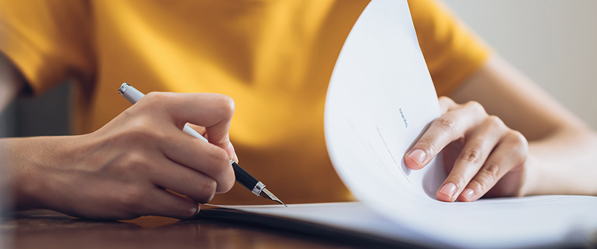 In a corporate law office, a person wearing a yellow shirt holds a pen and flips through a stack of papers on the desk.