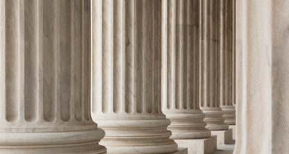 Close-up view of several large stone columns with vertical grooves, typical of classical architecture, lined up in a row—an elegant look often found at prestigious corporate law office entrances.