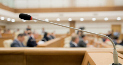 A close-up of a microphone in a conference room at a corporate law office, with blurred chicago lawyers seated in the background.