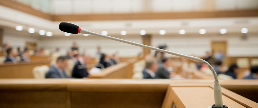 A close-up of a microphone in a conference room at a corporate law office, with blurred chicago lawyers seated in the background.