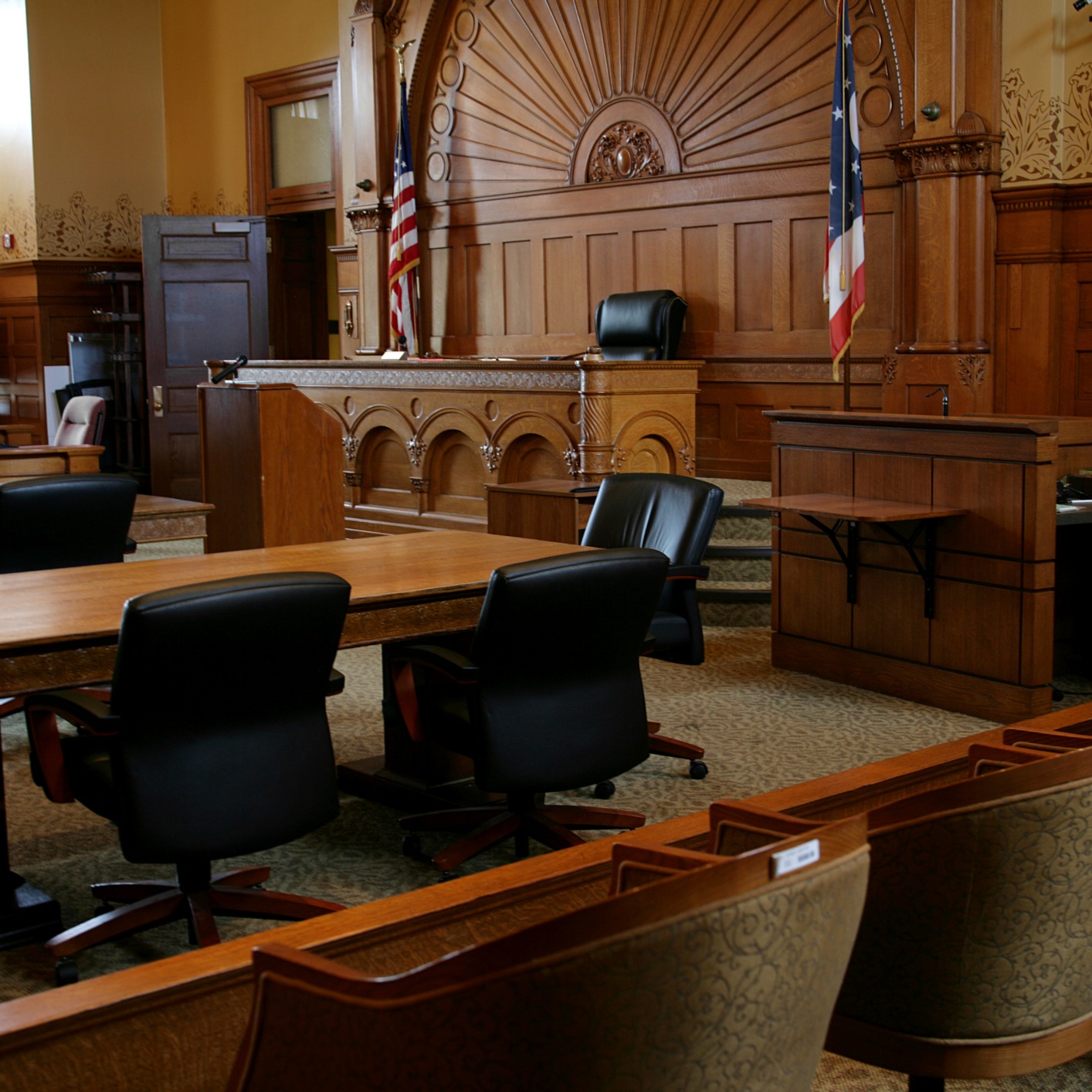 Empty courtroom with wooden benches, tables, chairs, a judge's bench, and American flags; no people present—an atmosphere where Chicago lawyers might debate intellectual property law.
